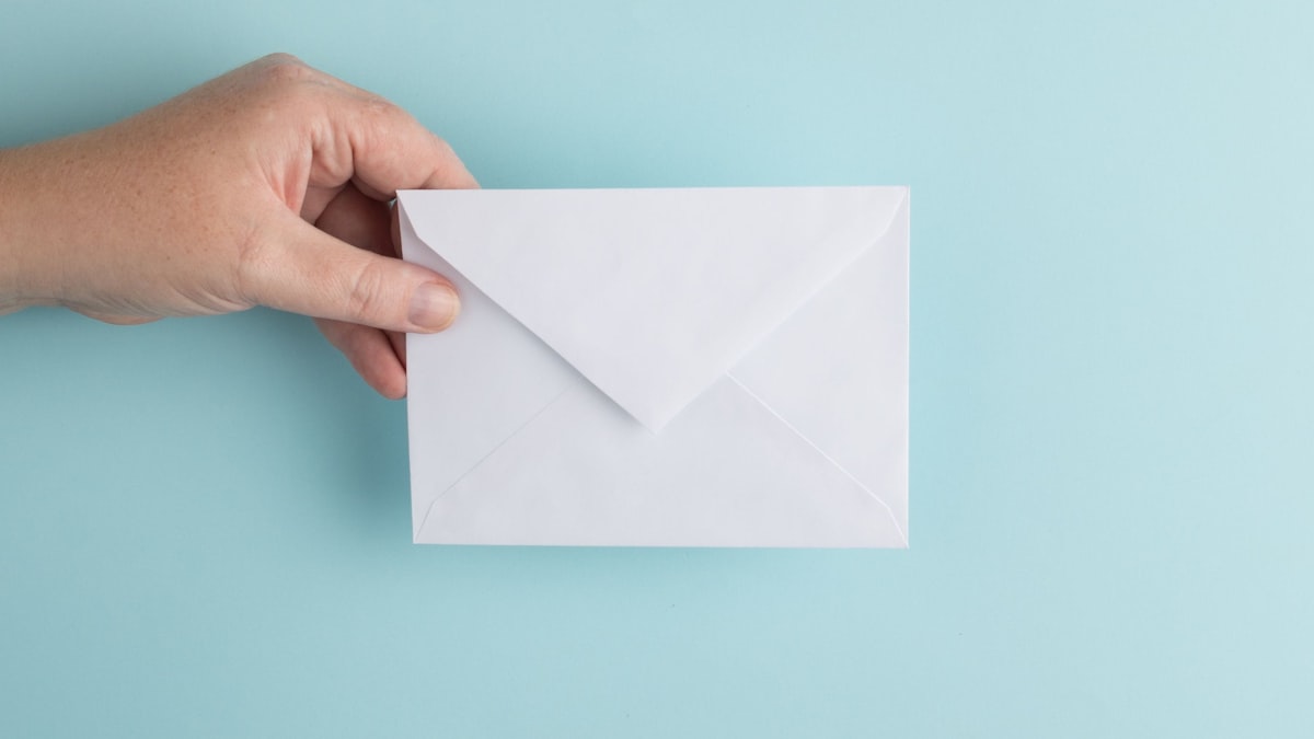 Person holding a white envelope — how spam filters treat file sharing links differently across Gmail, Outlook, and corporate mail